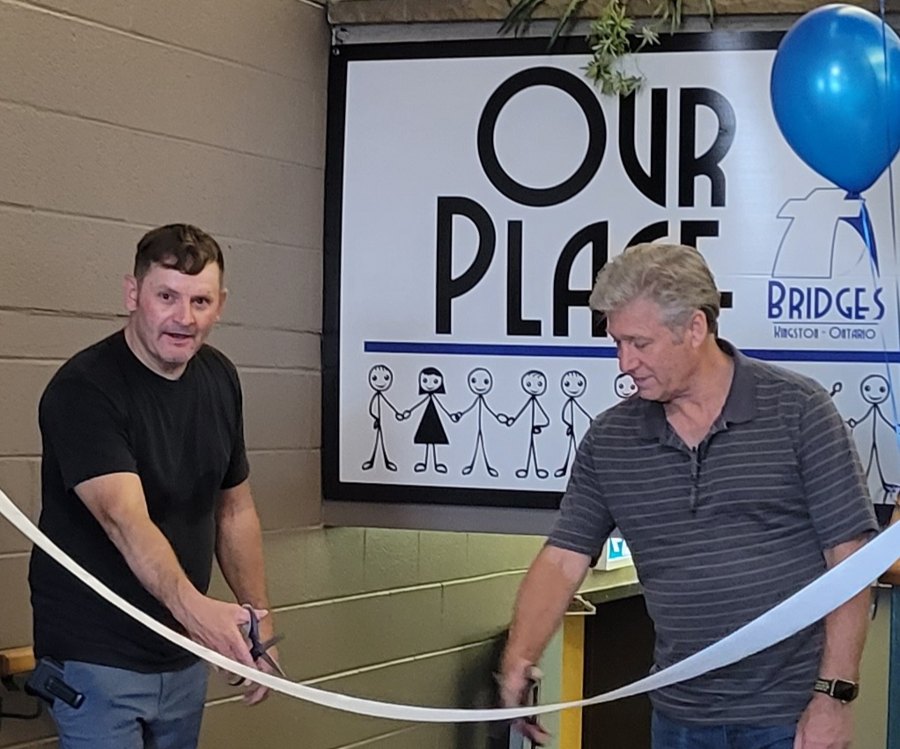 Two men cutting a ribbon in front of the Our Place sign at the grand opening