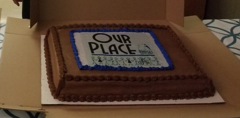 A chocolate cake decorated with the Our Place logo, made for the grand opening